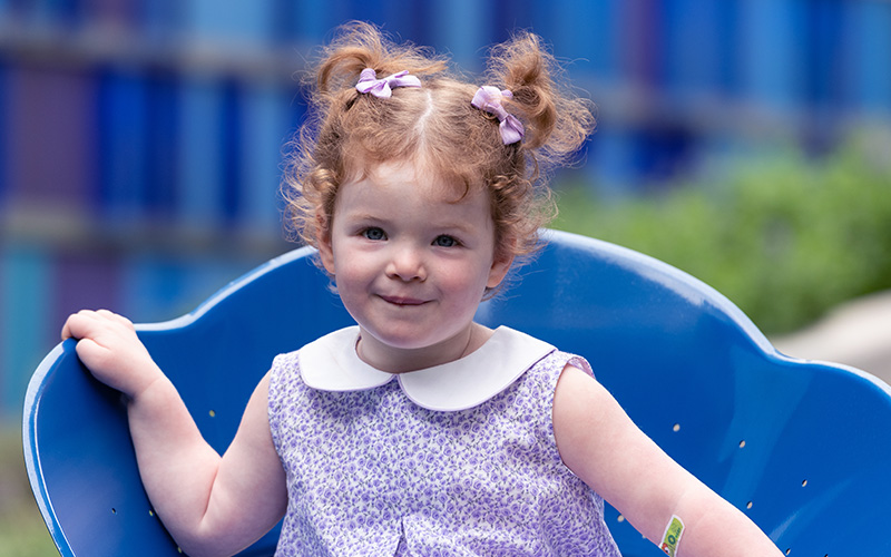 Young girl with red hair pulled up smiles while sitting down.