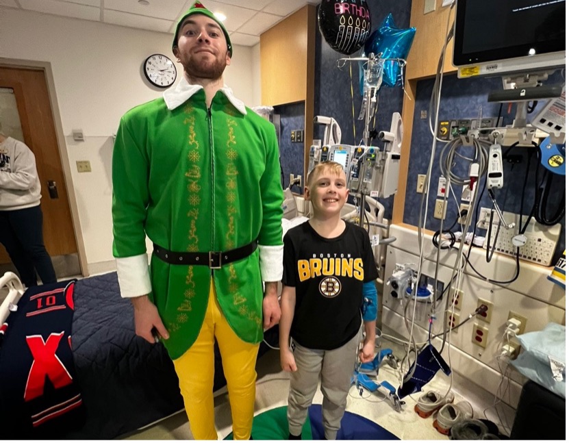 Bruins player Jeremy Swayman dressed in an elf costume stands with a Boston Children’s patient wearing a Bruins shirt