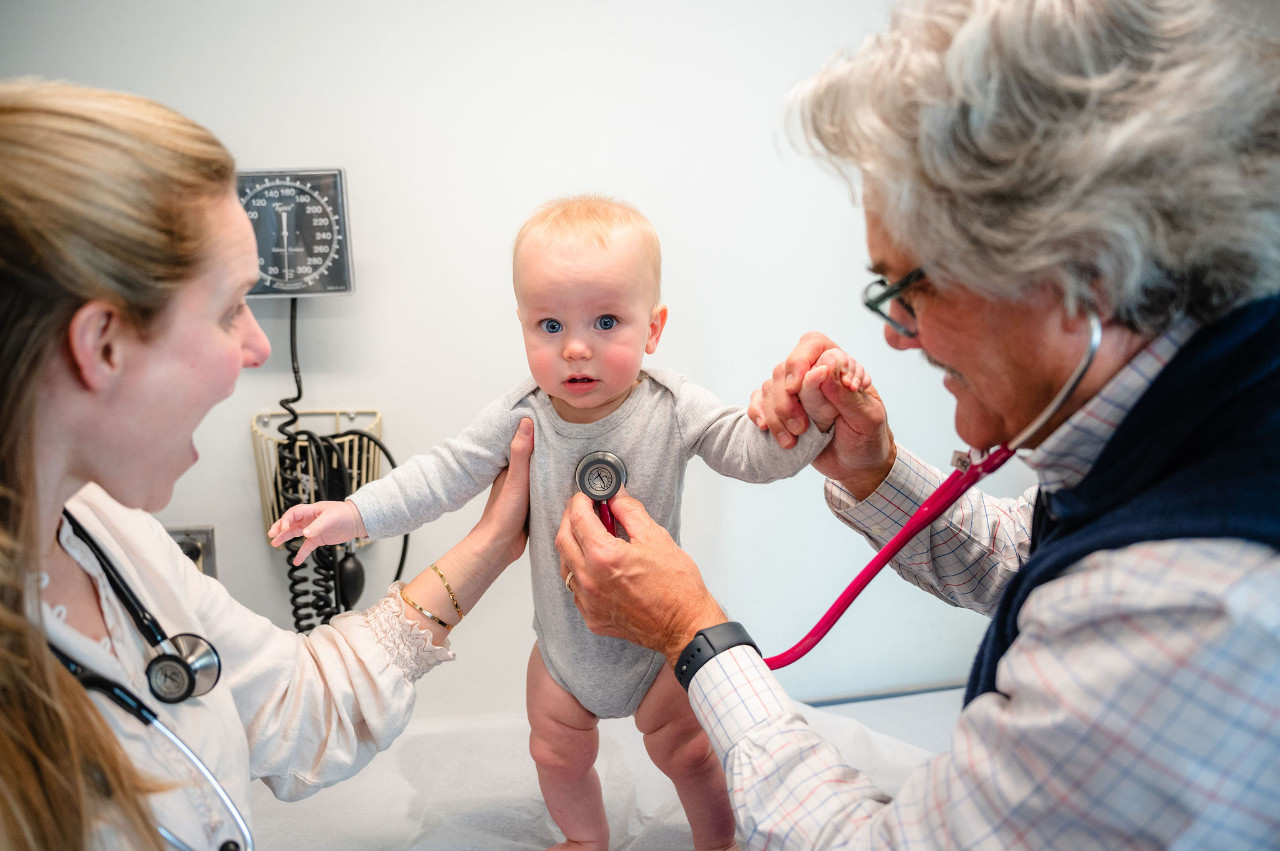 a baby looking at the camera as two medical professionals examine him