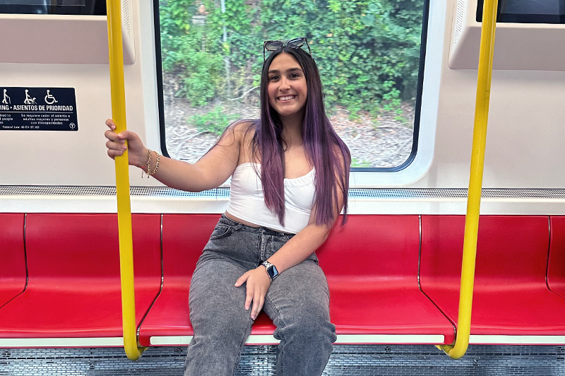 Teenager sits on train while holding onto pole