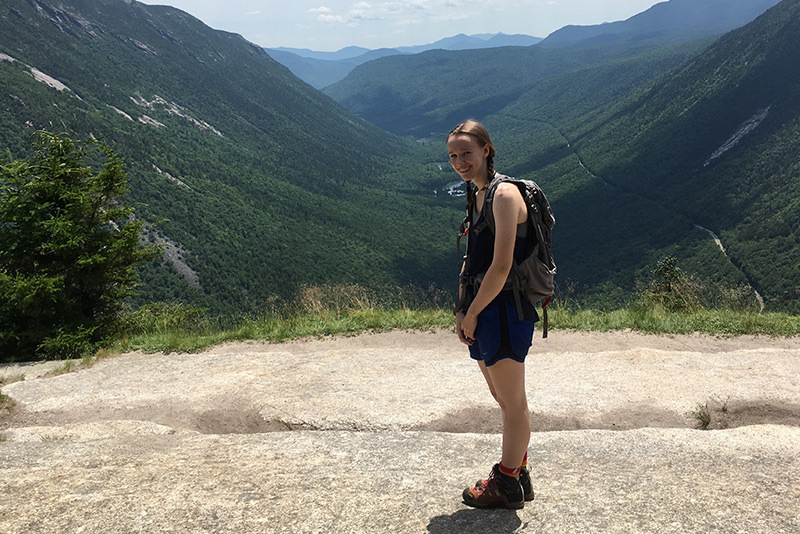 Young woman with backpack stands on mountain during hike