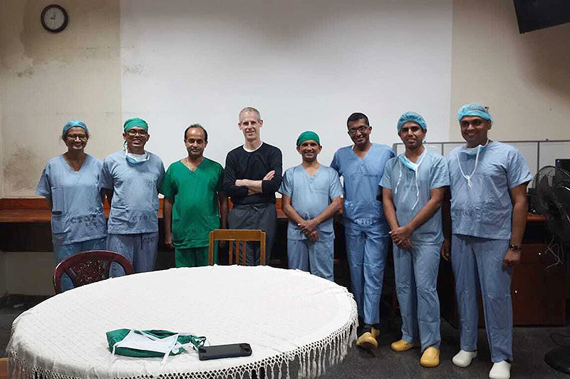 Clinicians wearing blue scrubs stand around man in black long-sleeve T-shirt