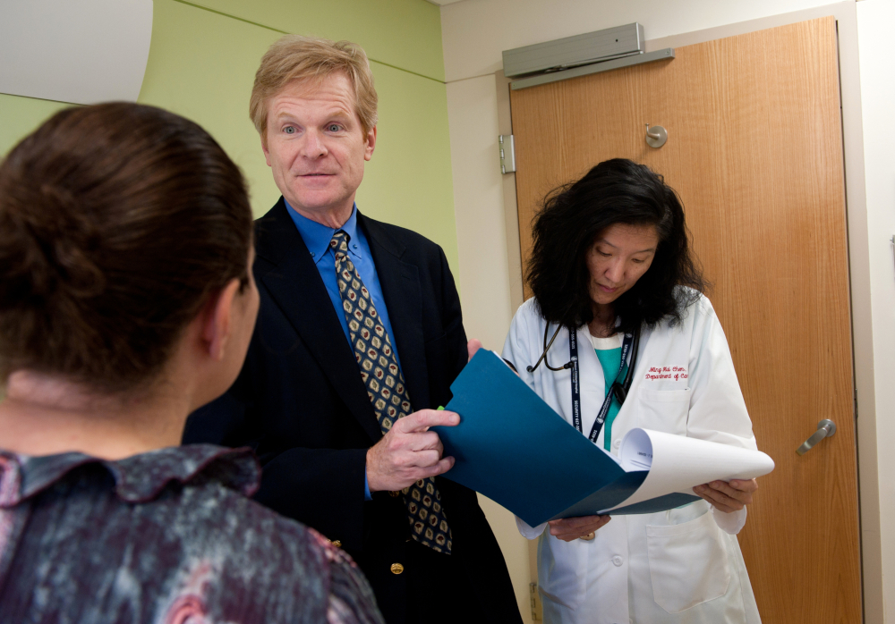 Man in suit, holding folder, and woman in doctor's coat, writing on notepad, speak with patient