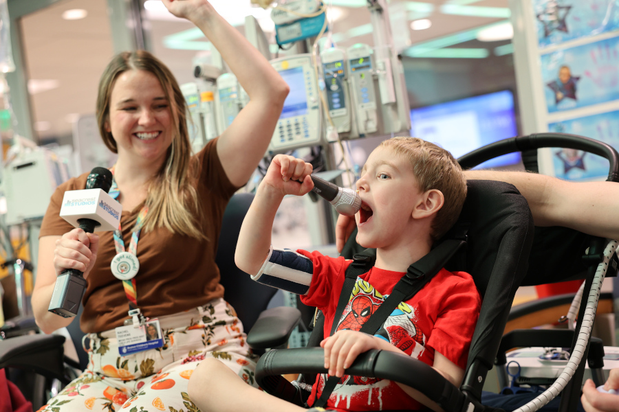 Woman holds left hand up in celebration as young boy sitting in wheelchair yells into microphone