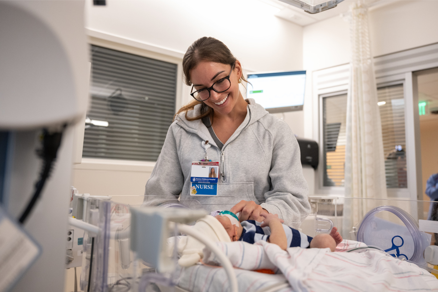 Woman wearing "NURSE" badge gently places left hand on young baby's chest.