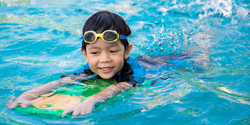Child plays in pool while using kickboard for support