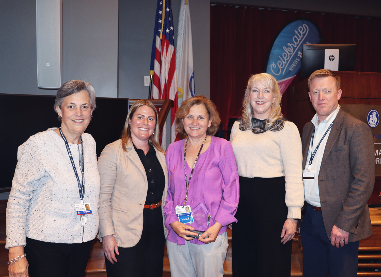 A group of four women pose on a stage in front of the american flag.