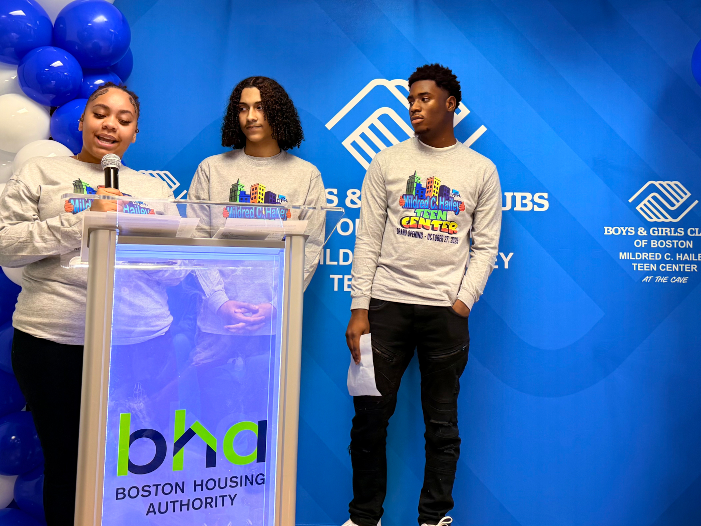 Three teens stand behind podium with Boston Housing Authority logo. One teen speaks.