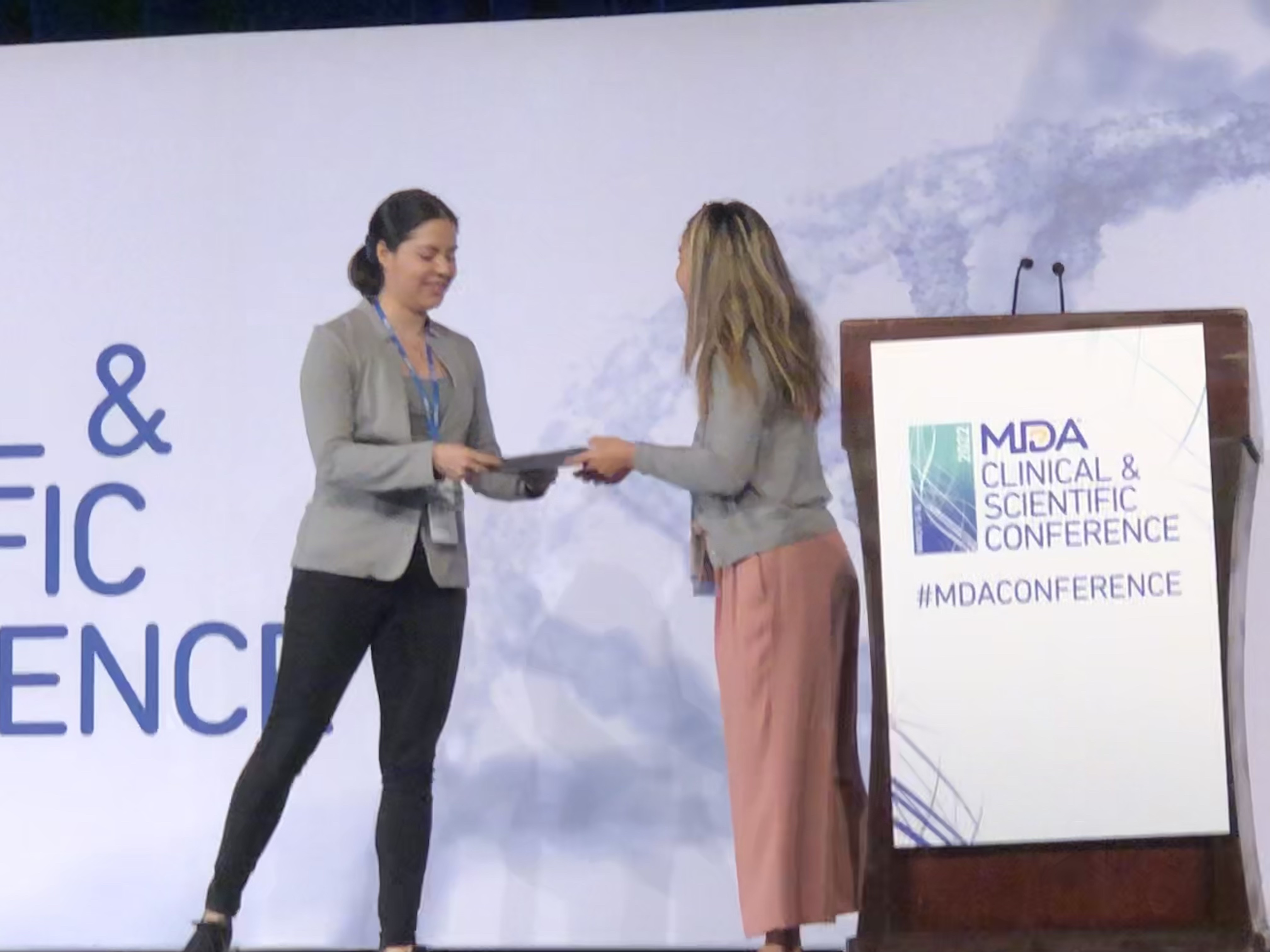 Two women shake hands on stage in front of a podium.