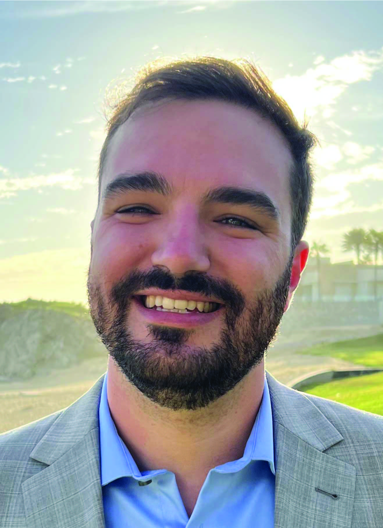 Headshot of Jake Jensen, a man with dark hair and beard stands outside and smiles at the camera.