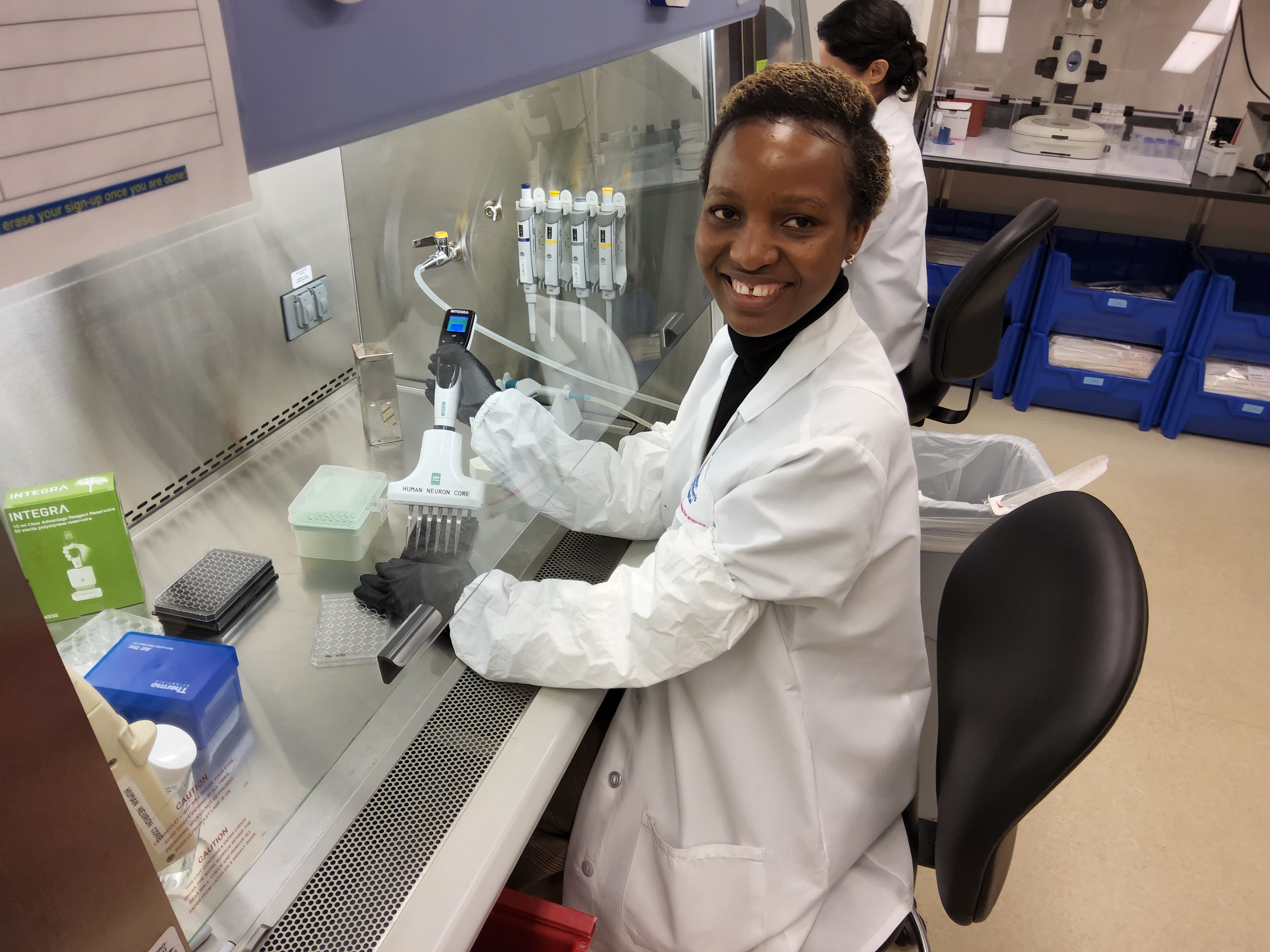 a black woman wearing a Boston Children's Hospital white lab coat fills pipettes at a lab station.
