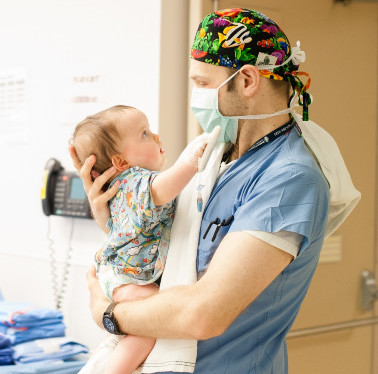male doctor in blue scrubs holding toddler