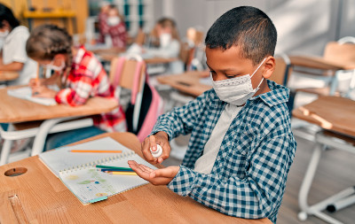boy in mask at school sanitizing his hands