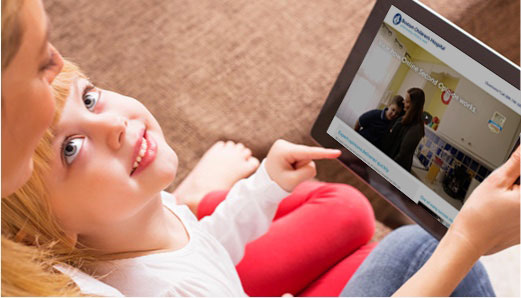 child sitting on a woman's lap, looking up from tablet and smiling.