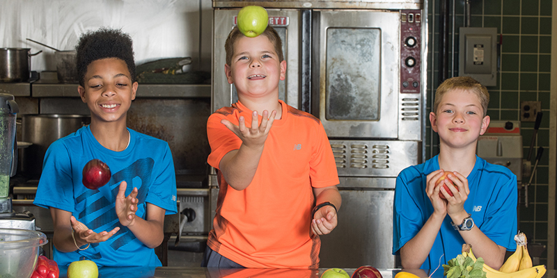 Three kids in a kitchen juggling fruit - obesity prevention