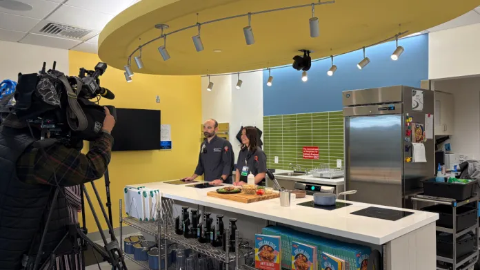 Camera crew films two adults standing behind kitchen island