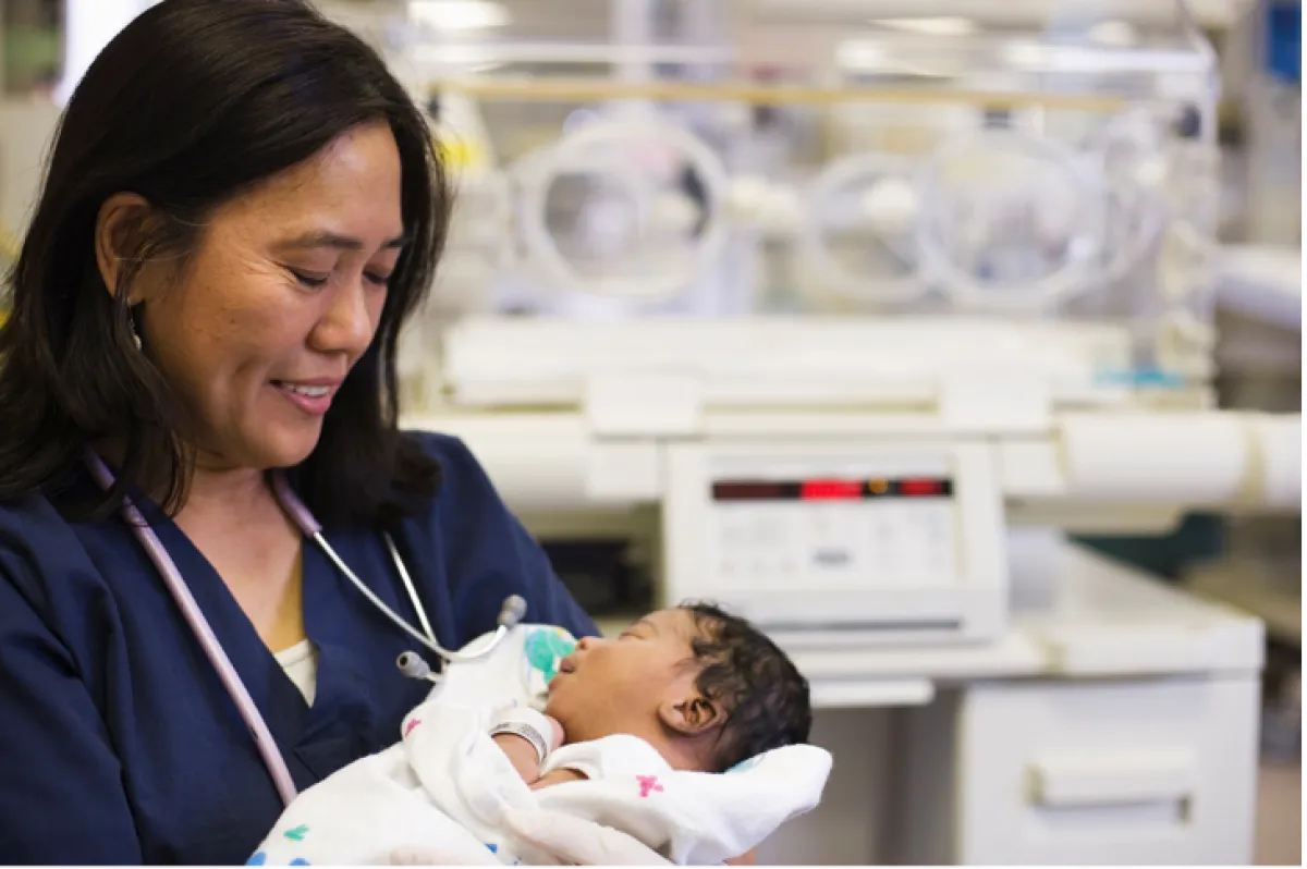 Woman clinician wearing stethoscope holds swaddled baby