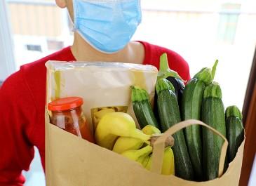 person in surgical mask carrying bag of groceries