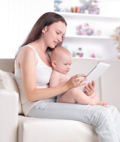 Woman holds baby on lap while using tablet