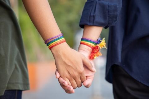 Teens wearing rainbow bracelets hold hands