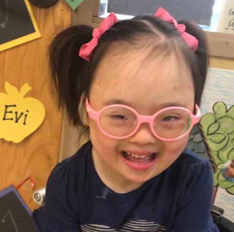 girl with pink glasses and hair in pig tails smiles at camera