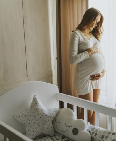 Pregnant woman holds stomach, stands in front of empty crib