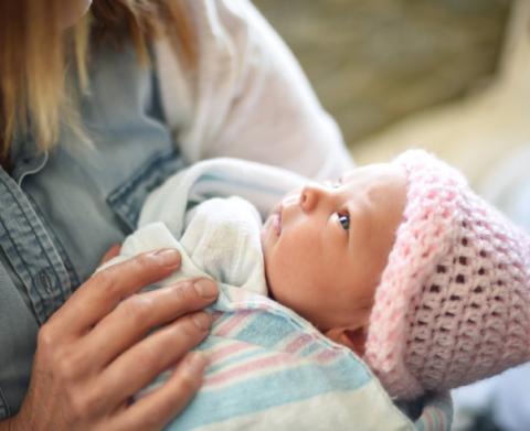 Woman holds baby swaddled in blanket and wearing a hat