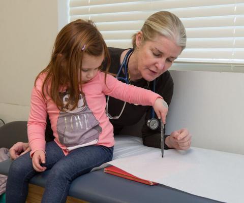 Girl draws on paper while clinician stands nearby