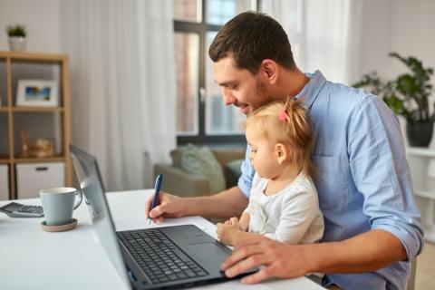 Father holds child on lap while working on laptop