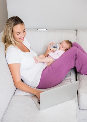 a mother feeding a baby in her lap while on the computer