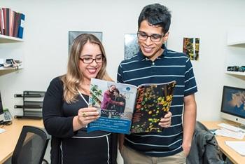 A blond woman and a dark haired man read a magazine together.