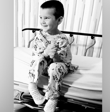 A boy wearing surgery scrubs sits on a recovery room bed