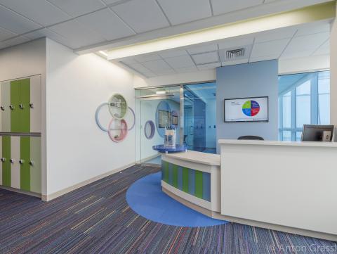 A large room at the hospital, with a white and green front desk, green and white lockers on the left side of the room, and colorful circle art on the wall.