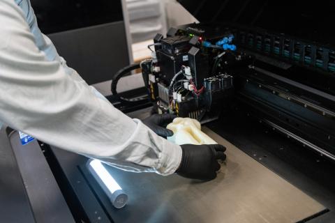 A white arm with a black glove uses a 3D printer to create a fake bone.