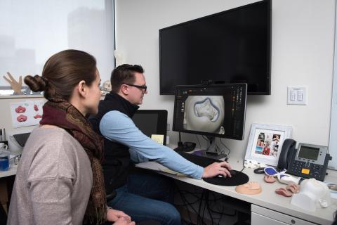 A man and a woman look at a brain image on a computer screen.