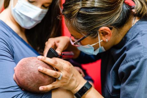 a mother holding her newborn while a pediatrician looks in his ear