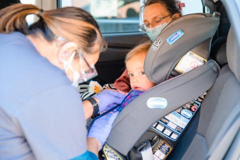 a pediatrician locking a child into a child seat in the backseat of a car