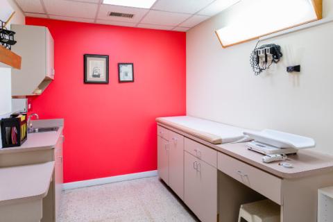 an empty pediatric exam room with a bright red wall