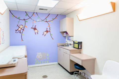 a pediatric exam room with a purple wall and decals of monkeys on vines