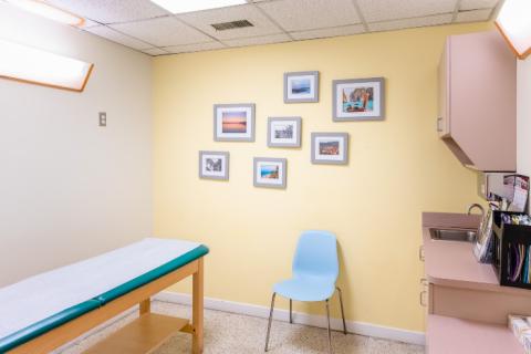 an empty pediatric exam room with seven pictures on a yellow wall