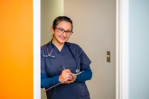 a woman medical provider stands in a doorway while holding a chart and smiling
