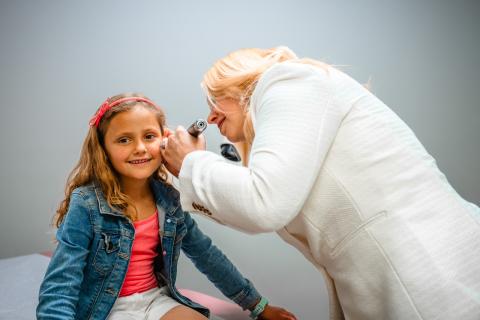 a girl smiling at the camera as she gets her ear examined by a female pediatrician