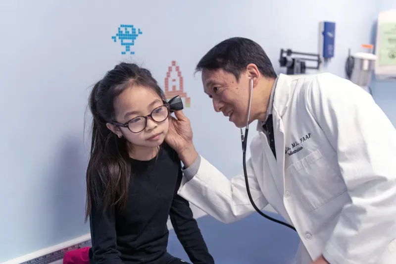 a pediatrician checking the ear of a young girl