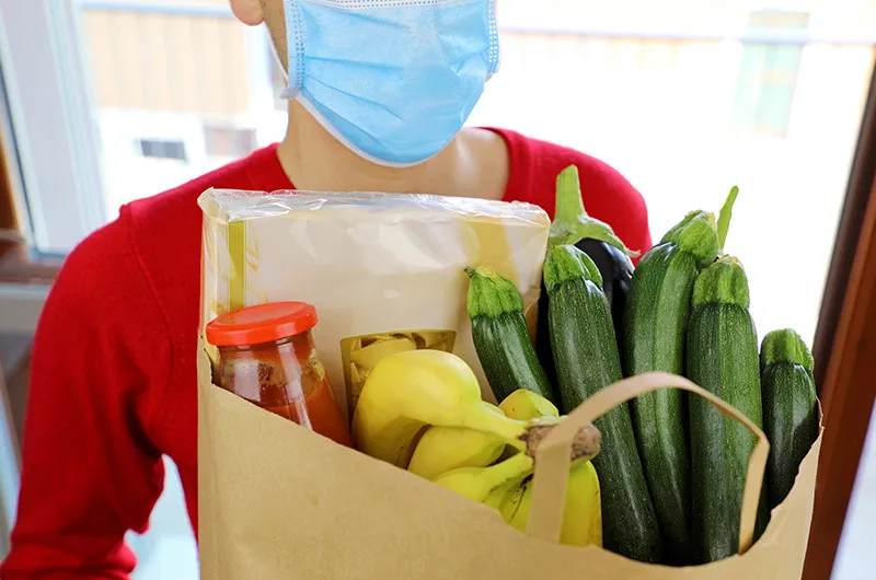 Adult wearing face masks holds large paper bag filled with various grocery items
