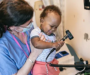 Clinician in scrubs holds child, and child holds medical device in their hands