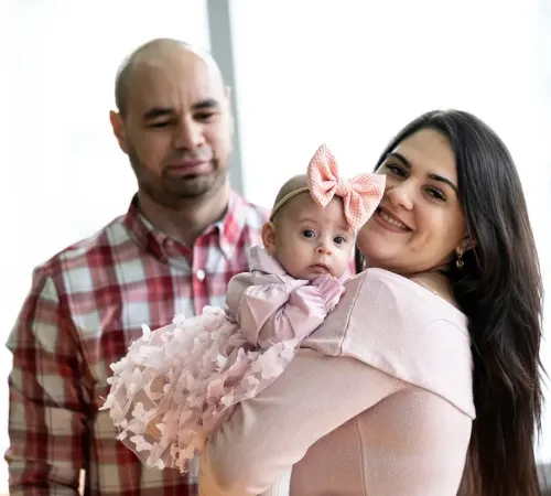 Woman holds baby girl as a man looks on.