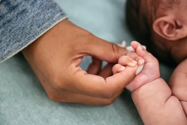 Adult holds tiny hand of newborn baby
