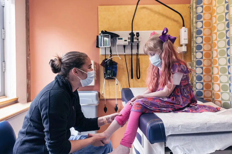 Clinician holds right leg of young girl visiting exam room