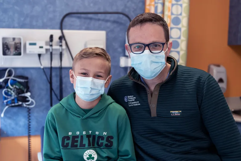 Boy wearing Celtics shirt and clinician in black jacket and glasses, both wearing facemasks