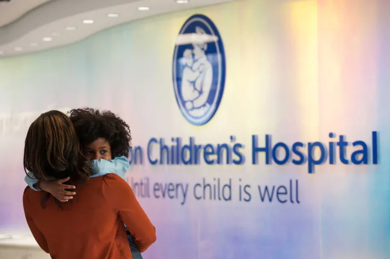 Mother holding child in front of Boston Children's Hospital logo in lobby